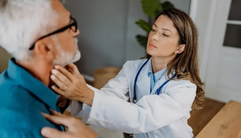 Une femme médecin examine le cou d'un homme âgé avec une barbe.