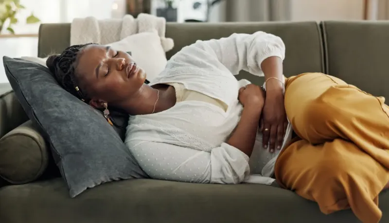 Une femme allongée sur un canapé, les mains sur le ventre, exprimant une douleur abdominale.