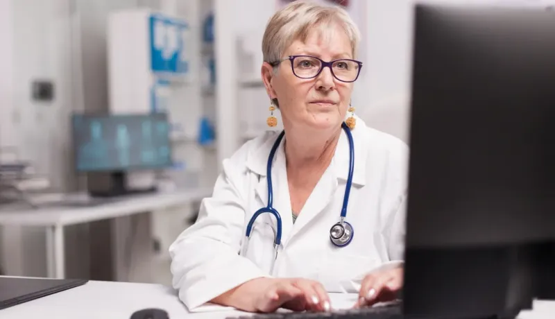 Une femme médecin âgée avec un stéthoscope travaille sur un ordinateur au cabinet.