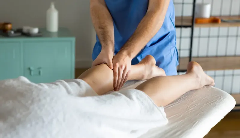 Un massothérapeute donne un massage des jambes à un patient allongé sur une table.
