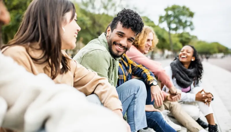Un groupe de jeunes amis souriants et riants assis ensemble à l'extérieur.