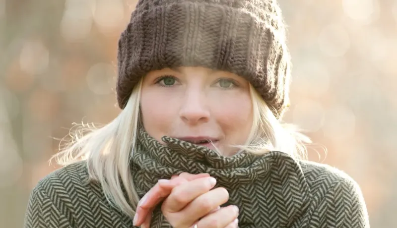 Gros plan sur une femme blonde souriante, emmitouflée dans un bonnet et une écharpe.