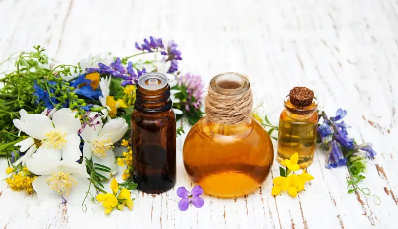 Bouteilles d'huiles essentielles ou végétales entourées de fleurs et d'herbes sur une table en bois.