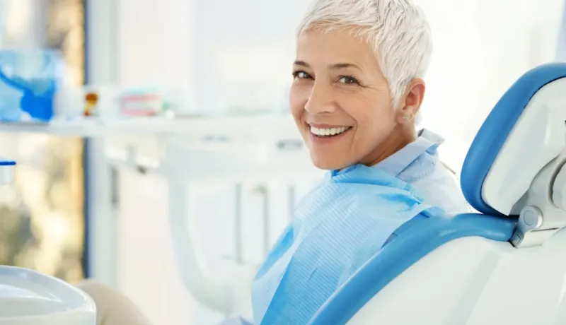 Une femme souriante aux cheveux courts gris dans un fauteuil de dentiste.