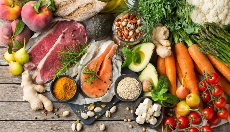 Vue de dessus d'une sélection d'aliments sains : viande, poisson, légumes, fruits, noix et huiles.