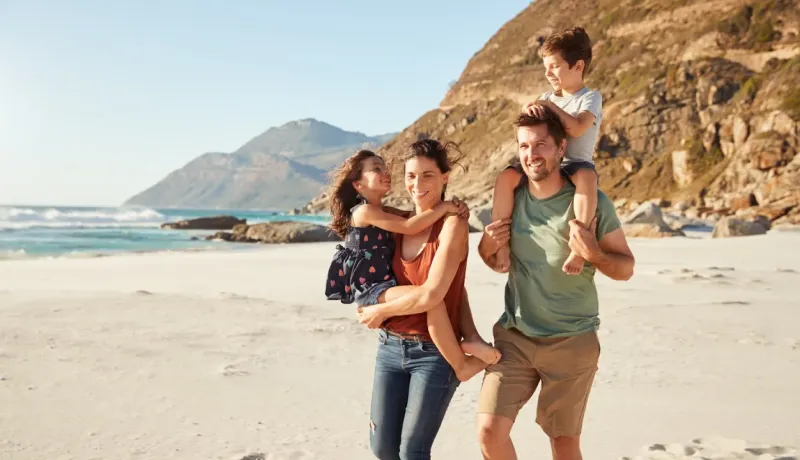 Une famille heureuse avec deux enfants marche sur une plage de sable, au bord de la mer.
