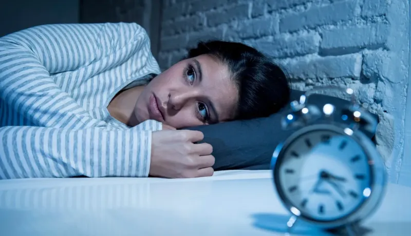 Une femme aux yeux ouverts est allongée dans son lit la nuit, observant un réveil, souffrant d'insomnie.