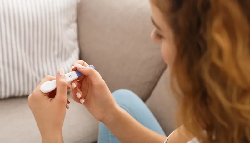 Gros plan sur une femme observant le résultat positif d'un test de grossesse à la maison.