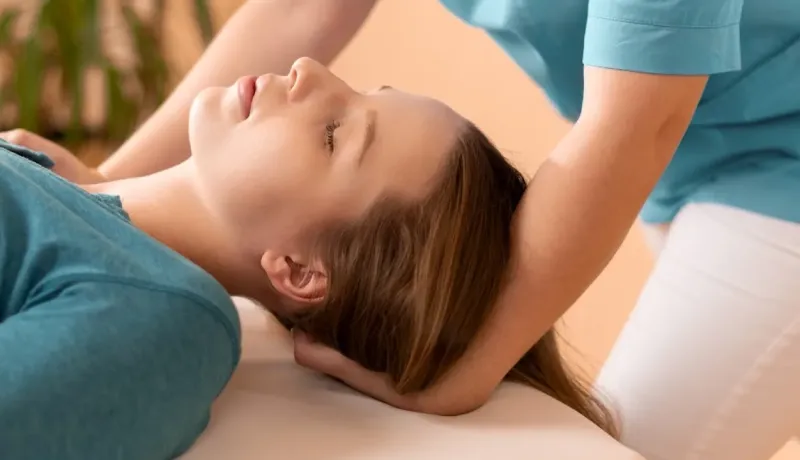 Une kinesitherapeute ajuste la tête et le cou d'une femme allongée, probablement lors d'une séance de chiropratique.