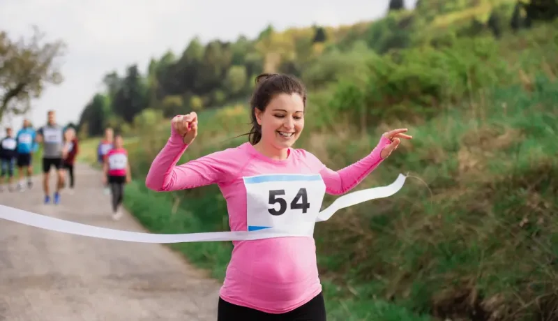 Une femme souriante franchit la ligne d'arrivée d'une course avec le dossard 54, les bras levés en signe de victoire.