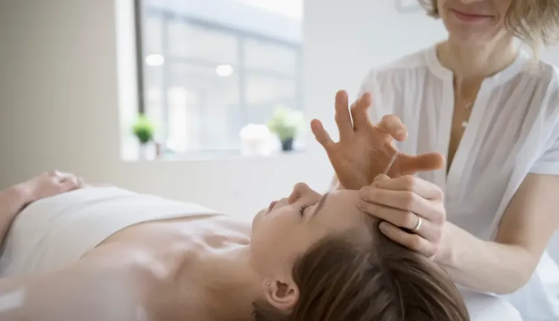 Une praticienne en médecine douce effectue une séance d'acupuncture sur le front d'une patiente allongée.
