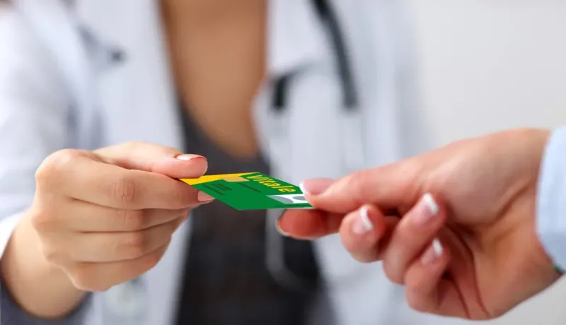 Gros plan sur une carte Vitale échangée entre un patient et un professionnel de santé en blouse blanche.
