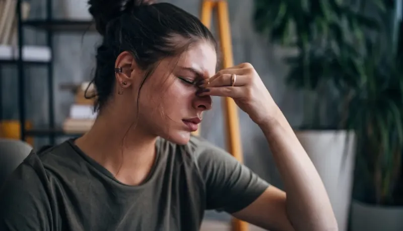 Une jeune femme serre l'arête de son nez, les yeux fermés, l'air souffrant ou fatigué.