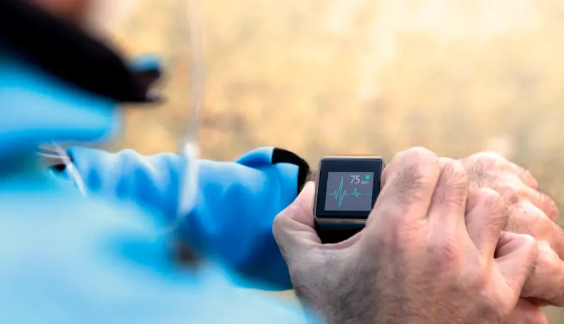 Un gros plan sur une montre connectée affichant un rythme cardiaque, portée par une personne en tenue de sport bleue.