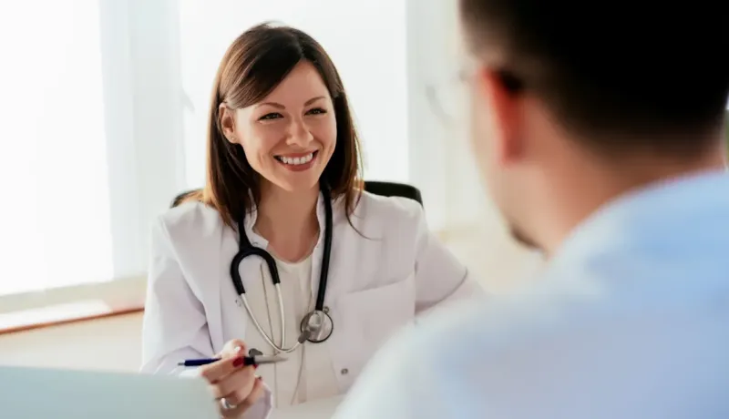 Une femme médecin souriante, stéthoscope autour du cou, discute avec un patient.