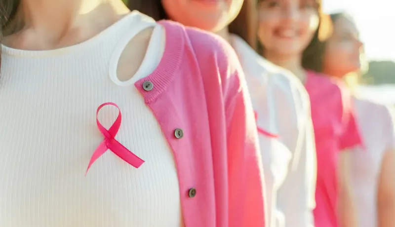Plusieurs femmes portant des rubans roses de sensibilisation au cancer du sein, souriant, focus sur la première.
