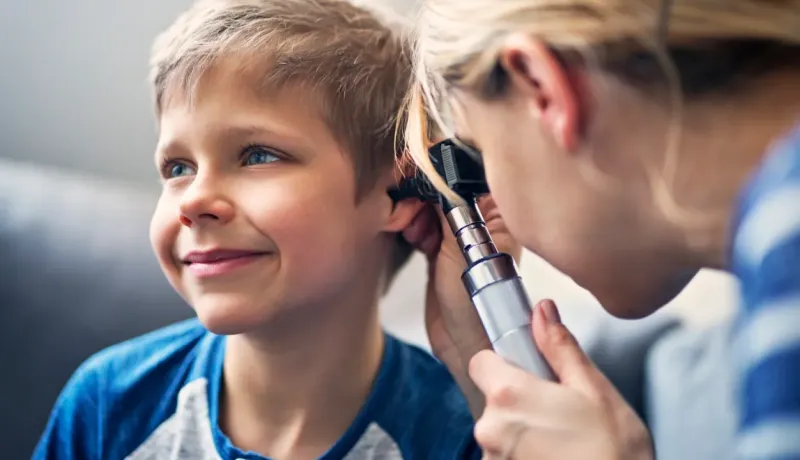 Un médecin examine l'oreille d'un jeune garçon souriant à l'aide d'un otoscope.