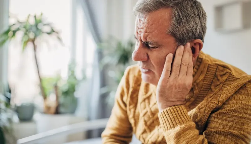 Un homme âgé se tient l'oreille d'un air douloureux, suggérant un problème d'audition ou une otite.