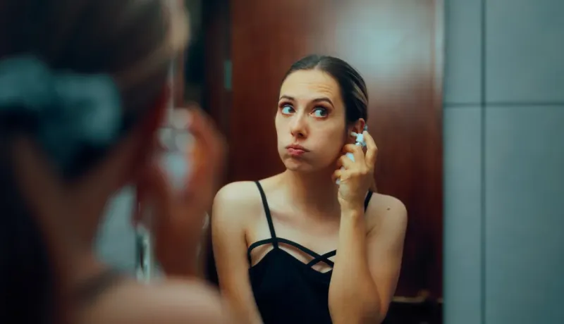Une jeune femme regarde son reflet dans le miroir en se nettoyant l'oreille avec un spray.