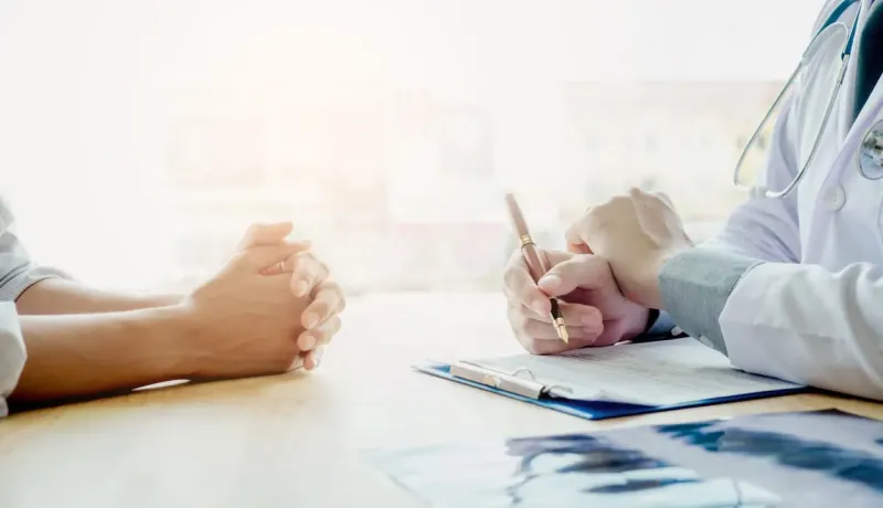 Médecin écrivant sur un presse-papiers face à un patient.