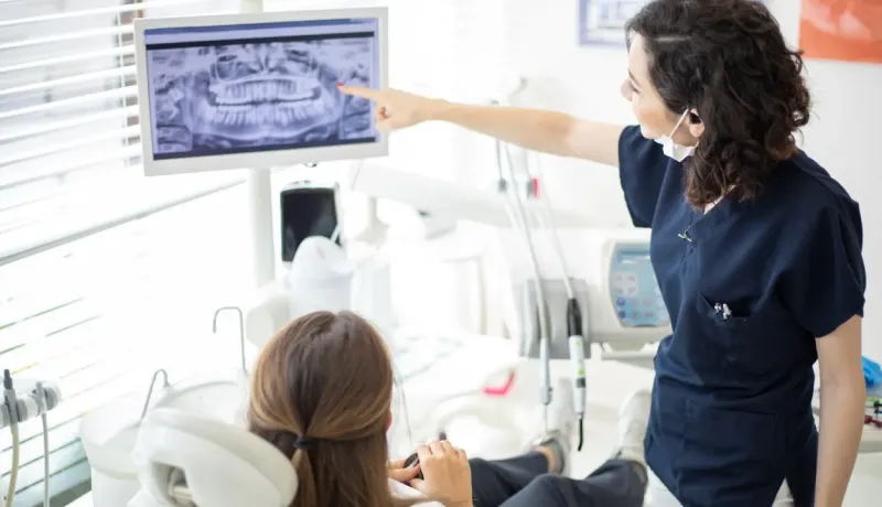 Une dentiste indique une zone sur une radiographie panoramique dentaire affichée sur un écran à une patiente.
