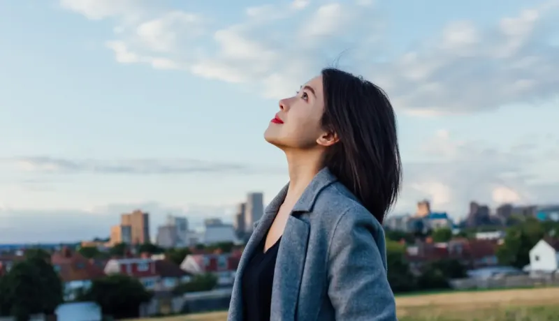 Une jeune femme regarde le ciel avec optimisme en milieu urbain, profitant d'un moment de calme.