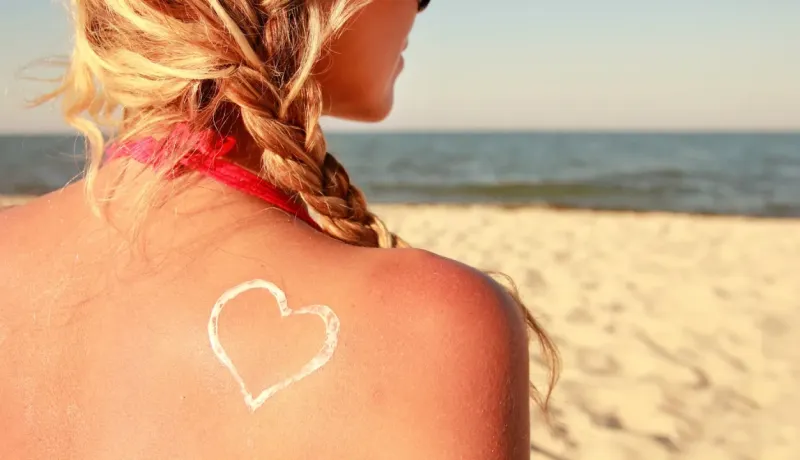 Gros plan sur le dos d'une femme sur la plage avec un cœur dessiné avec de la crème solaire, symbole de protection solaire.