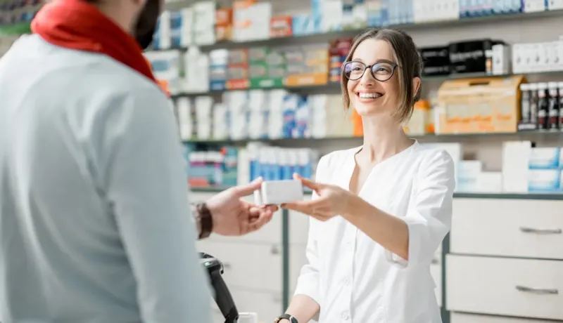 Une pharmacienne souriante tend une boîte de médicament à un client à l'officine.