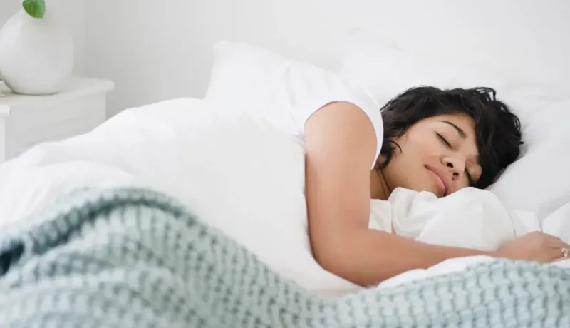 Une jeune femme dort paisiblement sous une couverture blanche et verte dans un lit confortable.