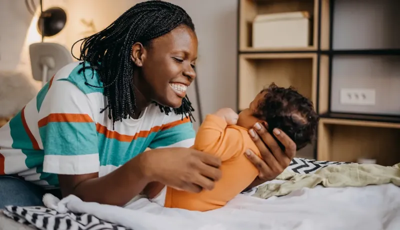 Jeune maman souriante jouant avec son bébé sur un lit.