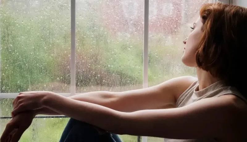 Femme pensive regardant par la fenêtre un jour de pluie.