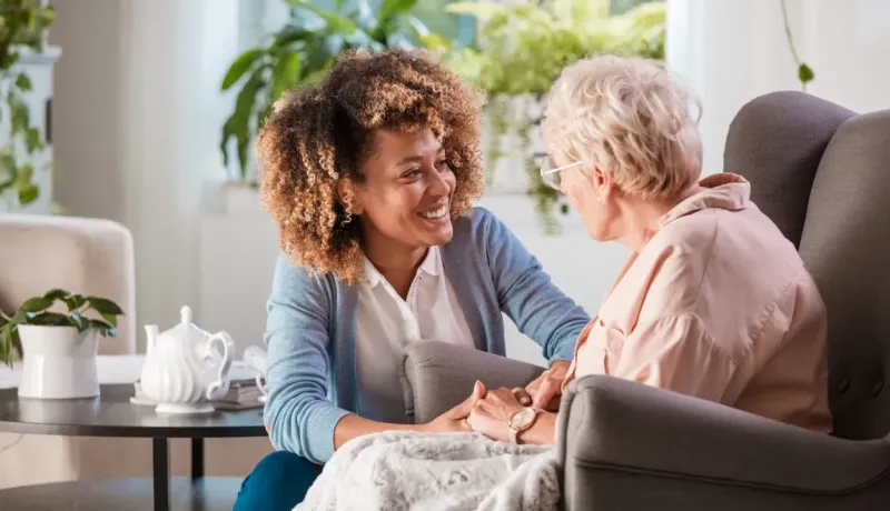 Auxiliaire de vie souriante tenant la main d'une personne âgée.