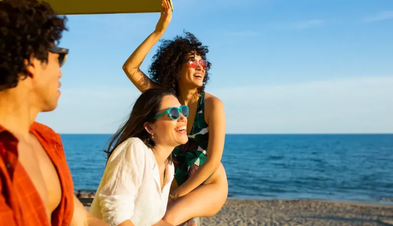 Amis souriants et lunettes de soleil sur une plage ensoleillée.