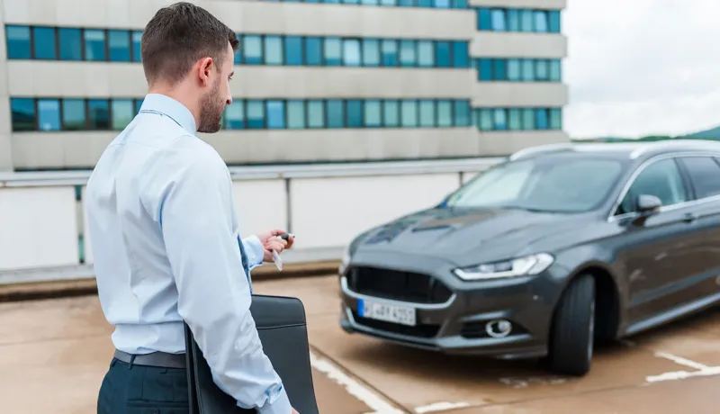 Un homme en costume d'affaires tenant une mallette, debout à côté d'une voiture.