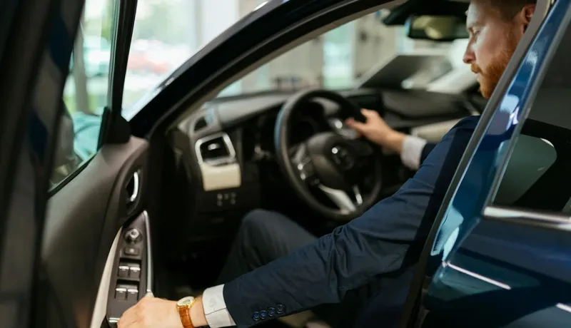 Un homme en costume est assis sur le siège conducteur d'une voiture.