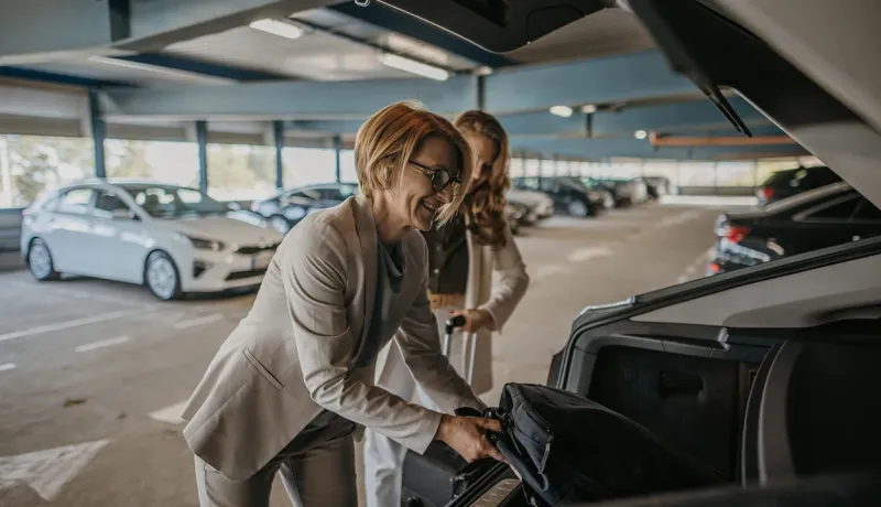 Deux femmes en tenue professionnelle rangent leurs valises dans une voiture.