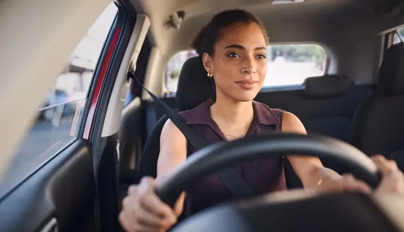 Jeune femme souriante et concentrée conduisant une voiture, ceinturée.