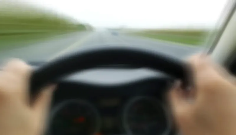 Des mains tenant un volant, vue floue d'une route en mouvement.