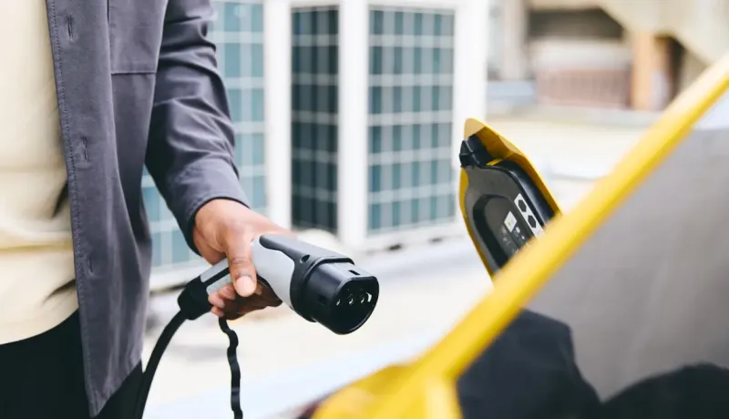 Une main tient une prise de recharge électrique pour une voiture jaune.