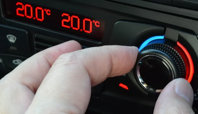 Gros plan d'une main ajustant un cadran de climatisation automobile affichant 20.0°C en rouge.