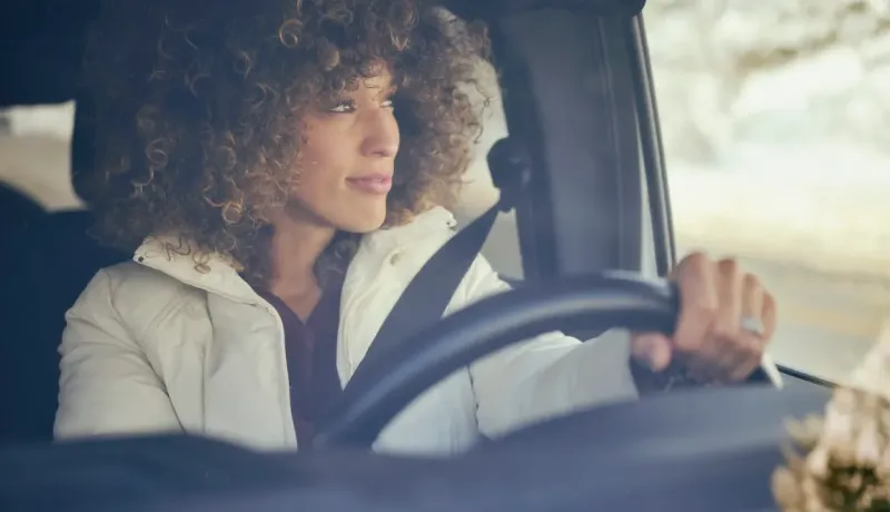 Une femme avec des cheveux bouclés conduisant une voiture.