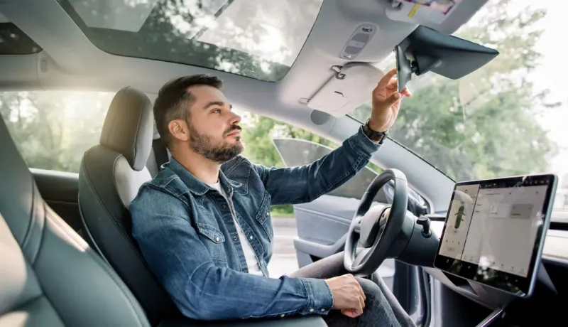 Un homme assis au volant d'une voiture moderne regarde dans son rétroviseur intérieur.