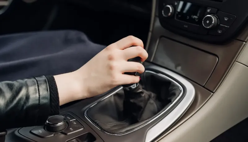 Gros plan d'une main changeant les vitesses sur un levier de vitesse manuel à l'intérieur d'une voiture.
