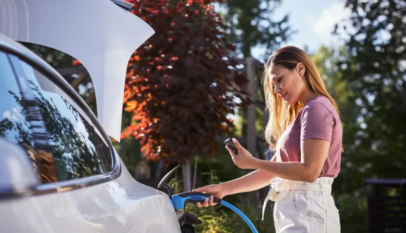 Une femme branche sa voiture électrique et regarde son téléphone.
