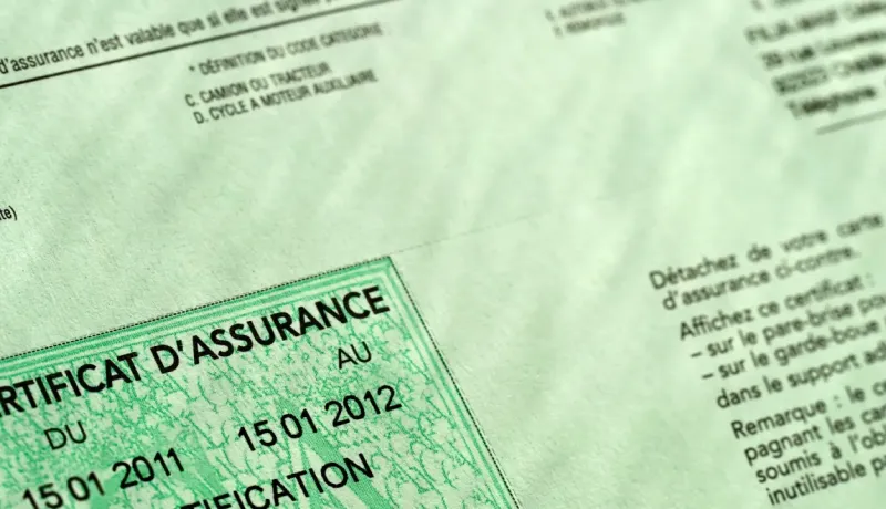 Gros plan sur un certificat d'assurance automobile vert affichant les dates de validité et des informations.