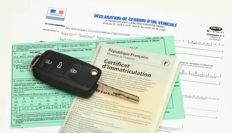 Une clé de voiture est posée sur des documents administratifs français, incluant un certificat d'immatriculation.