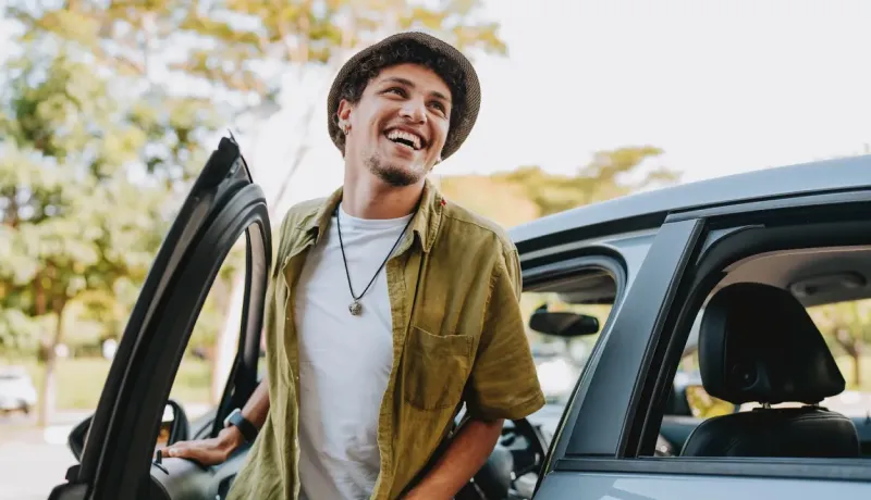 un jeune homme souriant sort de sa voiture.