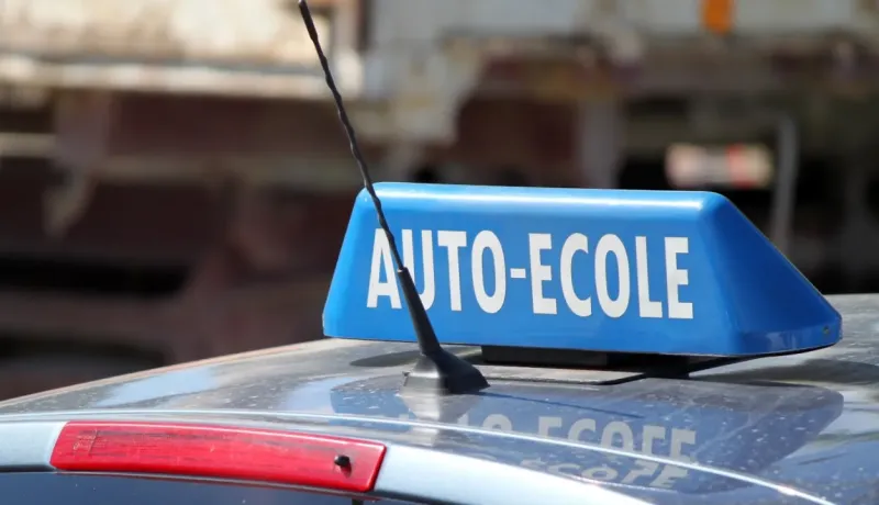 Gros plan d'un panneau bleu "AUTO-ECOLE" sur le toit d'une voiture, indiquant un véhicule d'auto-école.