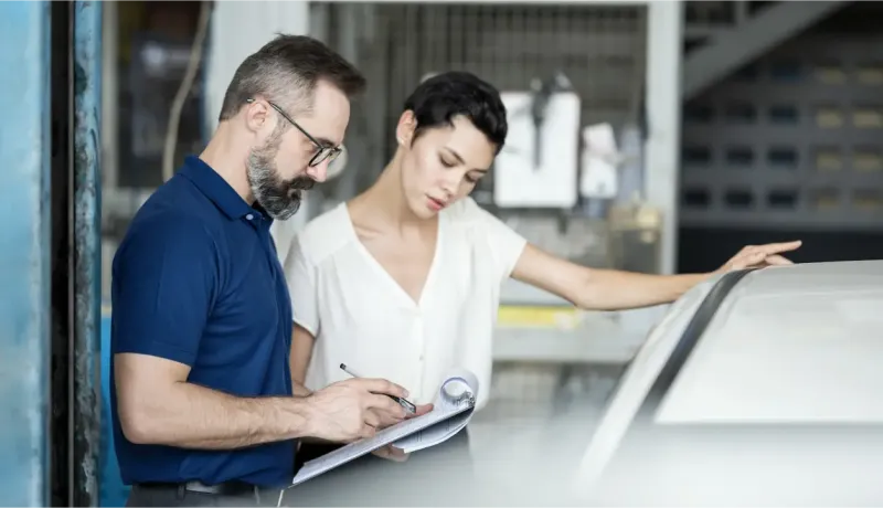 Un mécanicien et une femme regardent des documents près d'une voiture dans un garage.