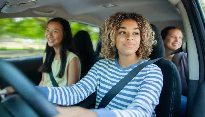Une femme souriante au volant, avec deux passagères en arrière-plan, lors d'un trajet en covoiturage.